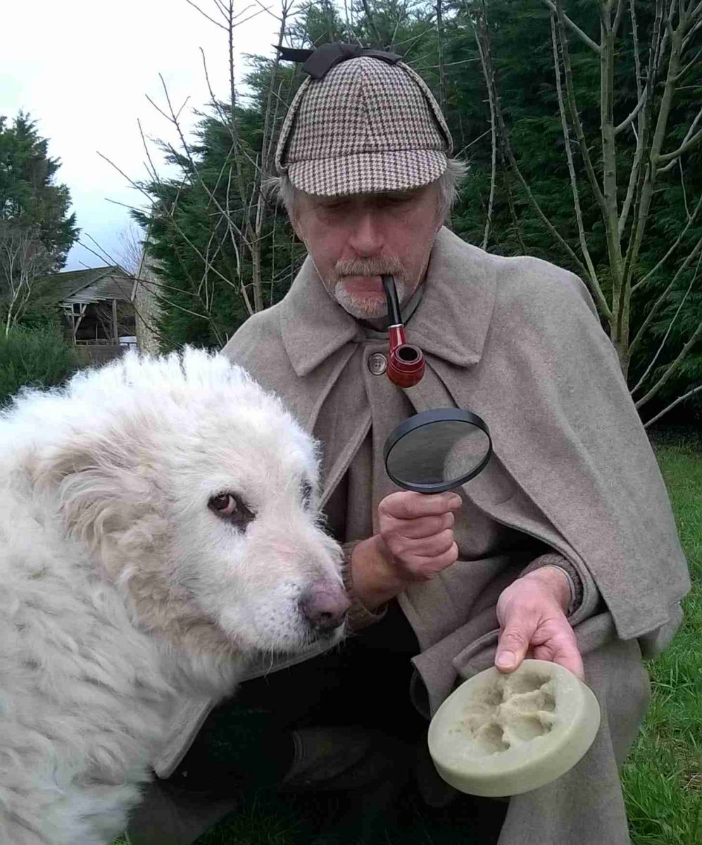 Détective anglais accompagné de son chien ayant une pipe et tenant dans l'une de ses mains une loupe et de l'autre une empreinte en argile.